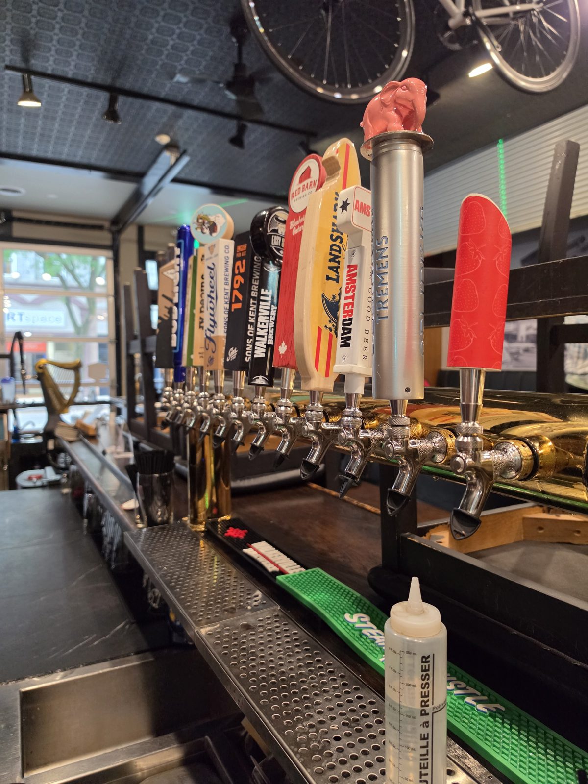 Long row of tap handles including Red Barn, Landshark, Walkerville, Sons of Kent, Amsterdam and Delirium Tremens, with a bike hung from the ceiling